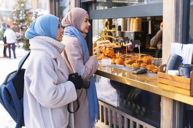two muslim women buying food from a pastry shop while traveling
